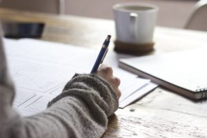 Parent sitting at a table alone with pen, papers and coffee, preparing for her manifestation determination meeting